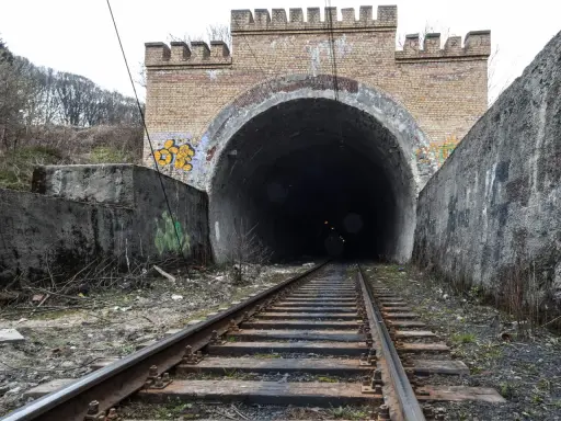 Torowisko prowadzi do ciemnego tunelu pod ceglanym łukiem z blankami, przypominającym bramę do dawnej kopalni Rydułtowy.