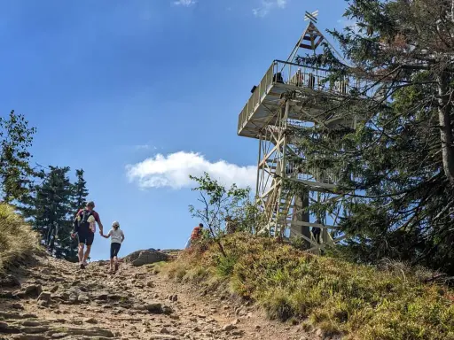 Rodzina wspina się kamienistym szlakiem na Baranią Górę, w tle widoczna wieża widokowa.