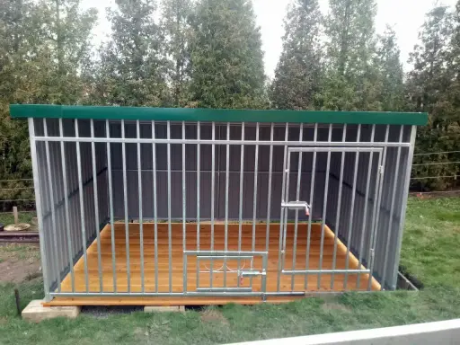 Solidny kojec dla psa z paneli ogrodzeniowych, z drewnianą podłogą i zielonym dachem. Idealne miejsce dla czworonoga.