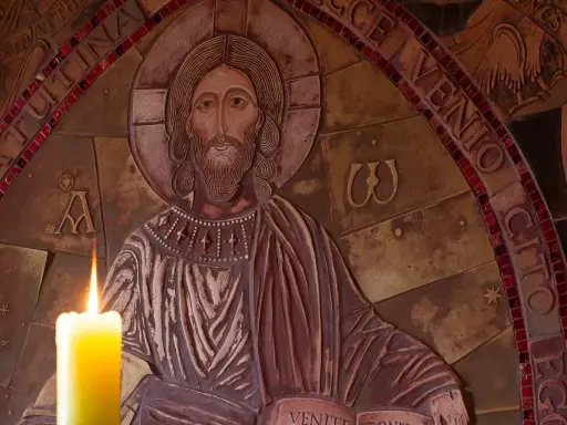 Płonąca świeca przed płaskorzeźbą Chrystusa, symbolizująca modlitwę o spokój i wyciszenie.
