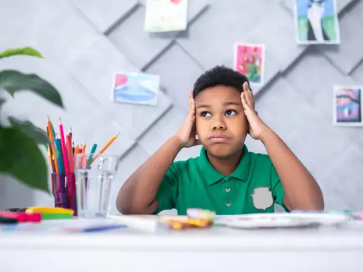 Niño frustrado con las manos en la cabeza, rodeado de materiales de arte, quizás lidiando con problemas de aprendizaje.