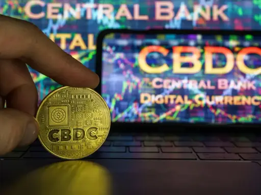 Złoty żeton CBDC w dłoni, symbolizujący cyfrowy pieniądz w Polsce. W tle ekran z wykresem i napisem "CENTRAL BANK DIGITAL CURRENCY".
