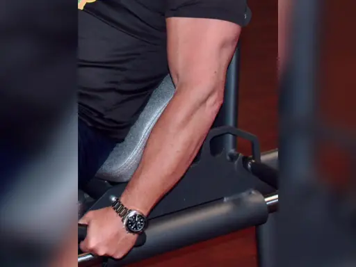 Mann trainiert unterarme im gym. Sein Bizeps ist gut sichtbar, während er sich auf ein Gerät stützt.