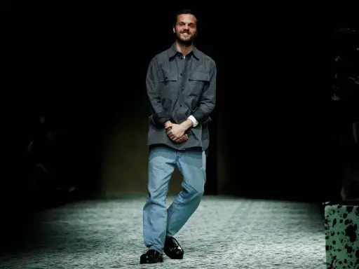 Matthieu Blazy, diseñador de Bottega Veneta, sonríe en la pasarela con camisa gris y vaqueros.