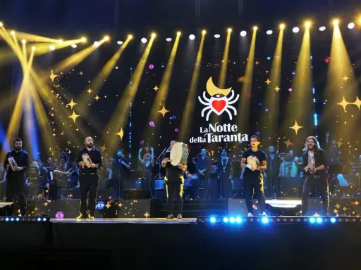 Artisti sul palco con tamburelli, orchestra e luci scintillanti per la sagra della taranta.