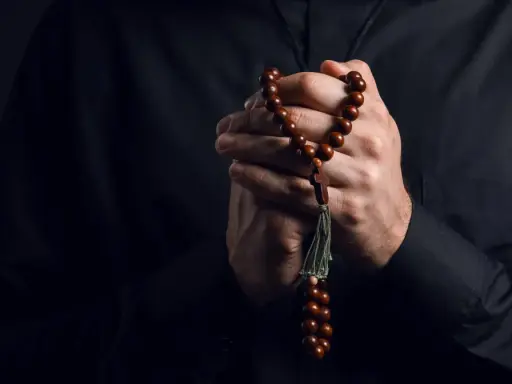 Dłonie księdza trzymające paciorki różańca, symbol wiary i nadziei w obliczu trudów życia, gdzie pańszczyzna a kościół splatały się w historii.