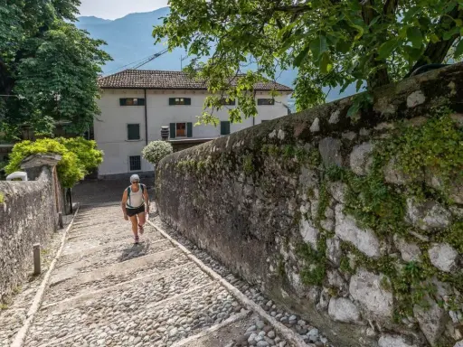 Una donna sale una scalinata di ciottoli verso un edificio bianco, un percorso che ricorda la salita alla Madonna della Corona.