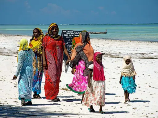 Kobiety w kolorowych strojach spacerują po plaży. Czy Zanzibar to kraj? Tak, to wyspa w Tanzanii.