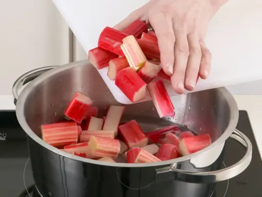 Rhabarberstücke werden von einem Schneidebrett in einen Topf mit Wasser geschüttet. So beginnt das Rhabarber verarbeiten für Kompott oder Kuchen.