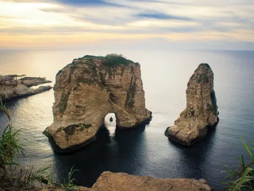 Felsformationen im Meer vor der Küste von Beirut Stadt, mit einem kleinen Boot, das durch den Felsbogen fährt.