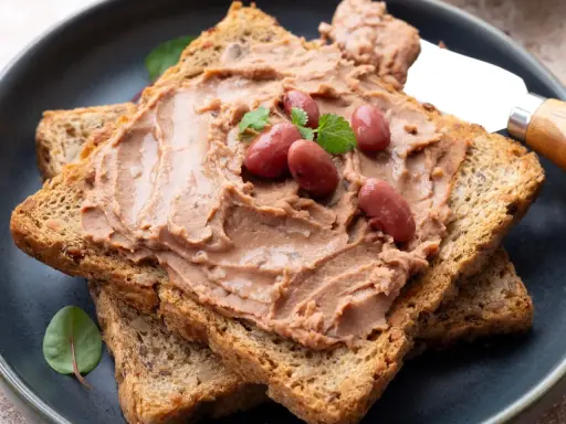 Pyszna pasta z czerwonej fasoli na chrupiących tostach, ozdobiona fasolkami i listkami ziół. Idealna na szybkie śniadanie.