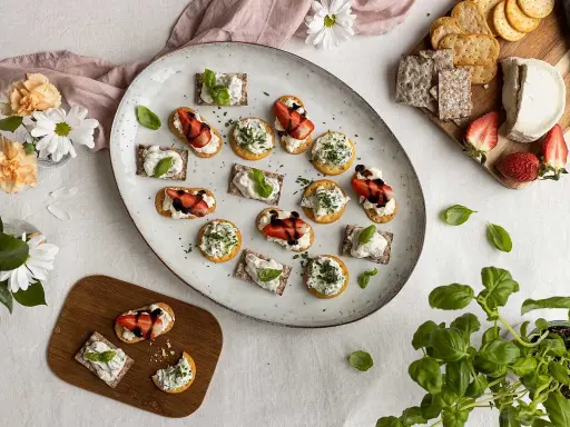 Vackra midsommar-snittar med ost, jordgubbar och örter på en stor tallrik. Perfekt för sommarfesten!