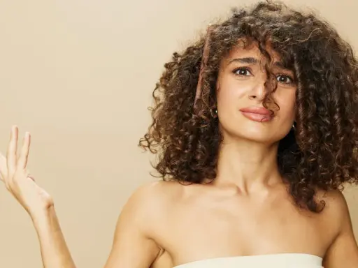 Une femme aux cheveux bouclés tente de diminuer le volume de sa chevelure avec un peigne.