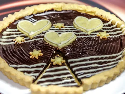 Una deliziosa crostata al cioccolato, decorata con cuori e fiorellini di pasta frolla, pronta per essere gustata.
