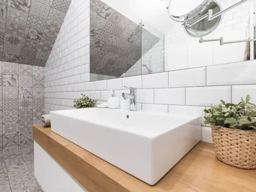 Salle de bain moderne avec lavabo rectangulaire, robinetterie chromée et un mur orné de **pose carrelage mural** patchwork gris et blanc.