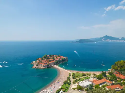Malownicza wyspa z czerwonymi dachami połączona z lądem, otoczona turkusowym morzem i piaszczystymi plażami. Czarnogóra plaże zachwycają.
