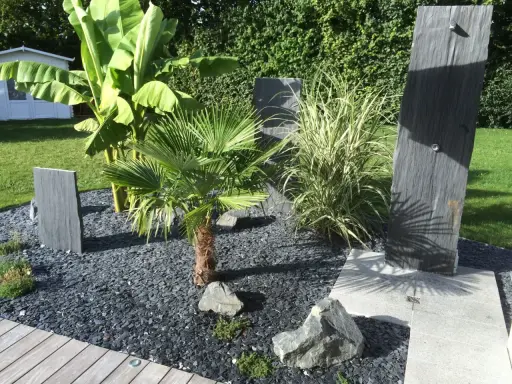 Une belle entrée de maison extérieure avec une plante luxuriante, des ardoises et un palmier.