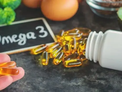 Dłoń trzyma kapsułki z kwasem omega 3. Obok leży buteleczka i tabliczka z napisem "Omega 3".