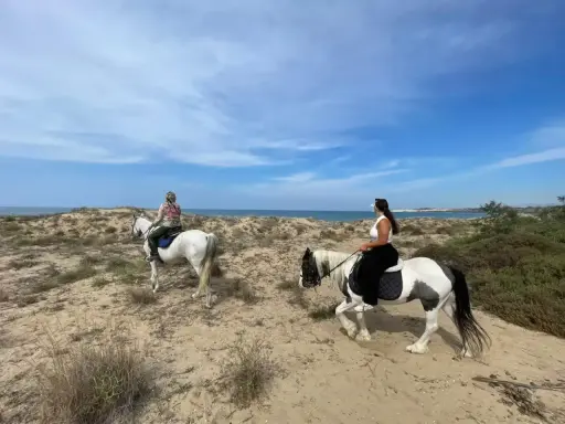 Due donne godono di una passeggiata a cavallo in Sicilia, tra dune sabbiose e il mare azzurro.