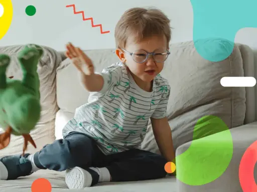 Un bambino super attivo gioca sul divano con un pupazzo verde. Le sue mani sono in movimento, pronto a interagire con il giocattolo.