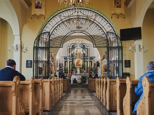 Wnętrze sanktuarium Matki Bożej Pięknej Miłości w Polańczyku. Wierni siedzą w ławkach, patrząc na ołtarz.