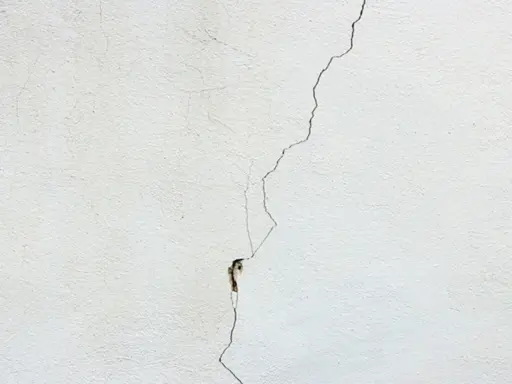 Una grieta fina y profunda recorre una pared blanca, mostrando diferentes tipos de grietas en techos y paredes.