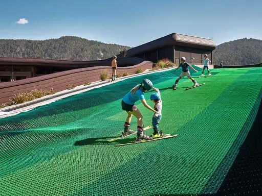 Bambini imparano a sciare su una pista verde al Falkensteiner Family Resort Lido, con montagne sullo sfondo.