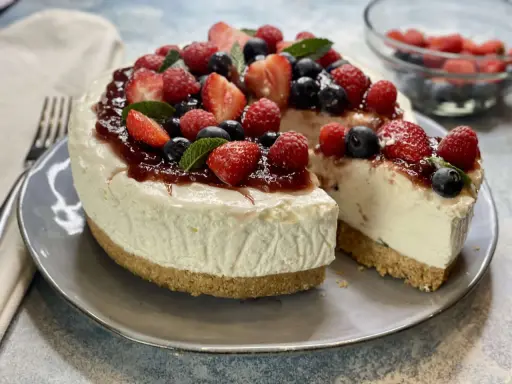 Deliziosa torta fredda allo yogurt, guarnita con fragole, lamponi, mirtilli e una colata di marmellata. Perfetta per un dessert estivo.