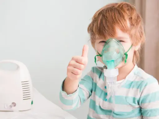 Chłopiec z gorączką i przyspieszonym oddechem używa nebulizatora, pokazując kciuk w górę.