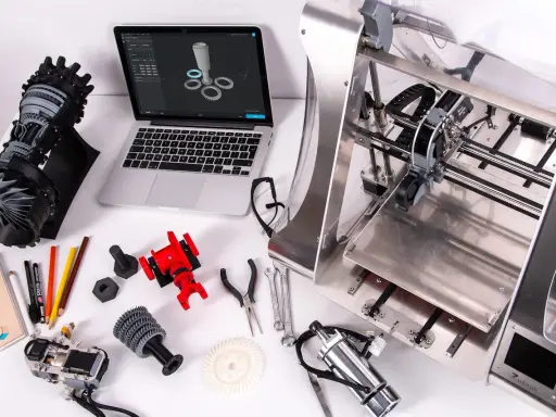 Il disegnatore CAD lavora su un laptop con un modello 3D, circondato da componenti stampati in 3D e strumenti.