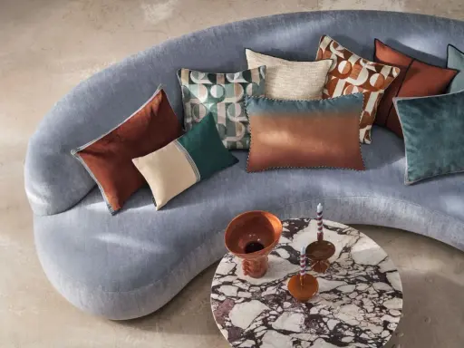 Tante idee cuscini divano: tonalità calde e fredde, fantasie geometriche e texture vellutate su un divano grigio.