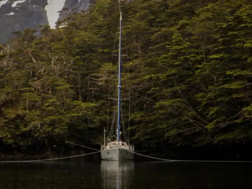 Voilier ancré dans un fjord, entouré d'une forêt dense. La chaîne du cablot, avec son épissure à 3 torons, assure la stabilité.