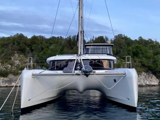 Ein moderner Katamaran mit zwei Rümpfen, der wie ein schwimmendes Haus aussieht, ankert vor einer bewaldeten Küste.