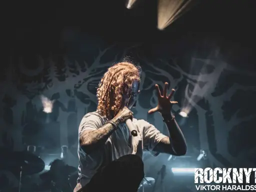 Lorna Shore Sverige: Sångaren med flammigt hår och tatueringar greppar mikrofonen på scenen, omgiven av rök och dramatiskt ljus.