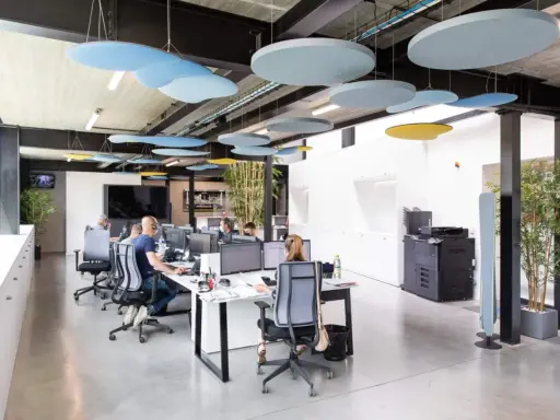 Bureau moderne avec des employés concentrés, des panneaux acoustiques colorés au plafond pour réduire le bruit au travail.