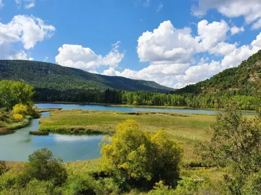 Paisaje de lagunas y montañas verdes, ideal para rutas senderismo Cuenca. Cielo azul con nubes blancas.