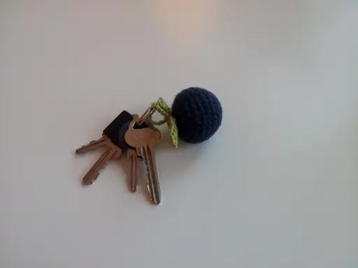 En mörkblå virkad nyckelring i form av ett bär, fäst vid ett knippe nycklar.