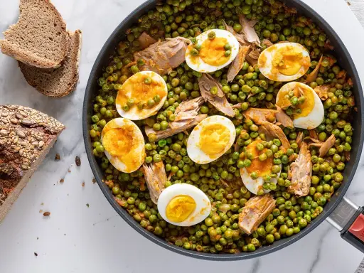 A skillet of peas and tuna with sliced hard-boiled eggs, served with bread.