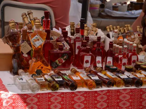 Różnorodne butelki z rakiją, w tym te w kształcie kobiecym, oferowane na targu. Co to rakija? To tradycyjny alkohol, często owocowy.