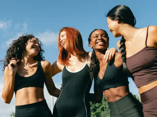 Quatre femmes souriantes, en tenue de sport, profitent du soleil. Leurs abdos sont visibles, suggérant une pratique comme l'abdo hypopressif.