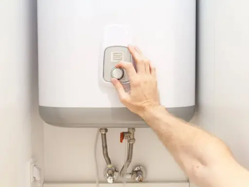 Mano ajustando el control de temperatura de un termo eléctrico. La instalación se ve limpia y moderna.