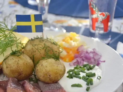 En klassisk midsommar meny med sill, färskpotatis, ägg, rödlök och gräddfil. En svensk flagga vajar stolt.