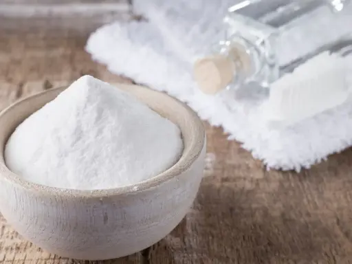 Soda oczyszczona w miseczce, obok ręcznik, buteleczka i szczoteczka. Czy soda oczyszczona odbarwia ubrania?