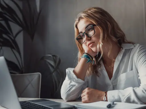 Zamyślona kobieta przy laptopie, z podpartą głową na dłoni. Wokół niej panuje atmosfera rezygnacji, jakby mówiła sobie: "nie mam marzeń".