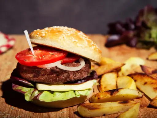 Burger maison avec pain aux graines, tomate, oignon, fromage et salade. Accompagné de frites. Une recette pain burger sans gluten à essayer !