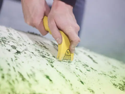 Mains utilisant un grattoir électrique antifouling pour enlever des résidus verts sur une surface.