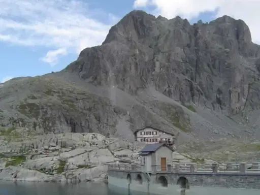 Rifugio sul lago della Vacca, con imponente parete rocciosa alle spalle.