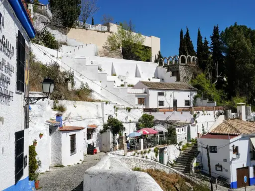 Weiße Häuser und Terrassen im Sacromonte, Granada, mit Kopfsteinpflaster und blühenden Pflanzen.