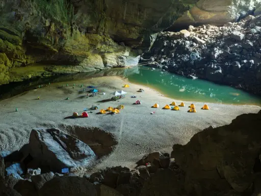 Obóz w jaskini Son Doong: namioty rozbite na piaszczystej plaży nad turkusową wodą, otoczone skalnymi ścianami.
