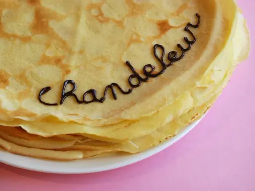 Une pile de crêpes dorées, décorées avec du chocolat formant le mot "Chandeleur". Un délice pour célébrer qu'est-ce que la Chandeleur.